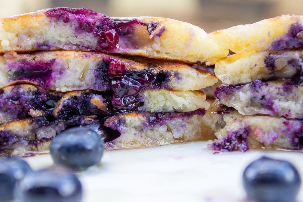 stack of lemon blueberry pancakes on plate cut in half showing inside with lots of blueberries