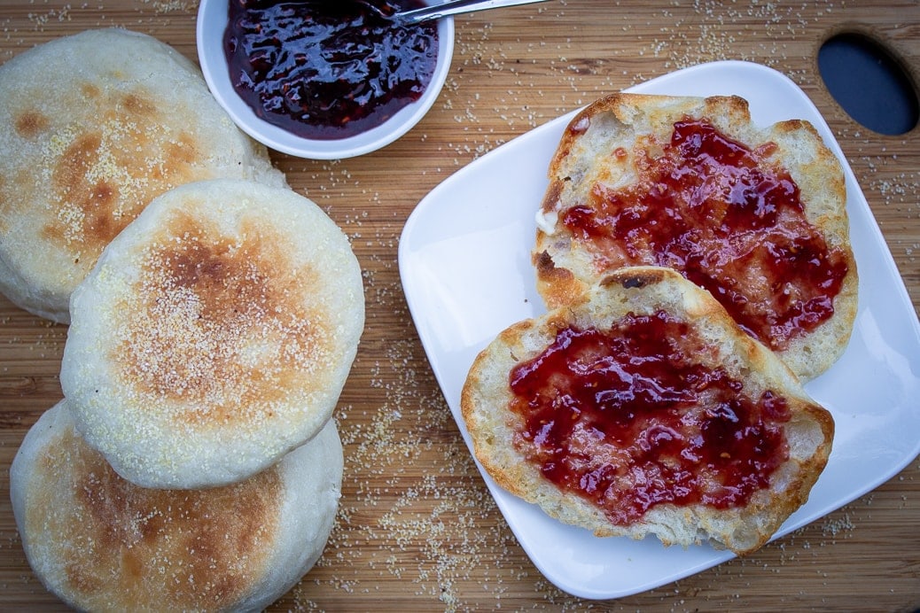 toasted english muffin with jam and butter beside 3 whole muffins and dish of jam