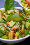 close up of mixed noodles, veggies, shrimp, garnish and dressing in bowl p