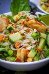 close up of mixed noodles, veggies, shrimp, garnish and dressing in bowl p1