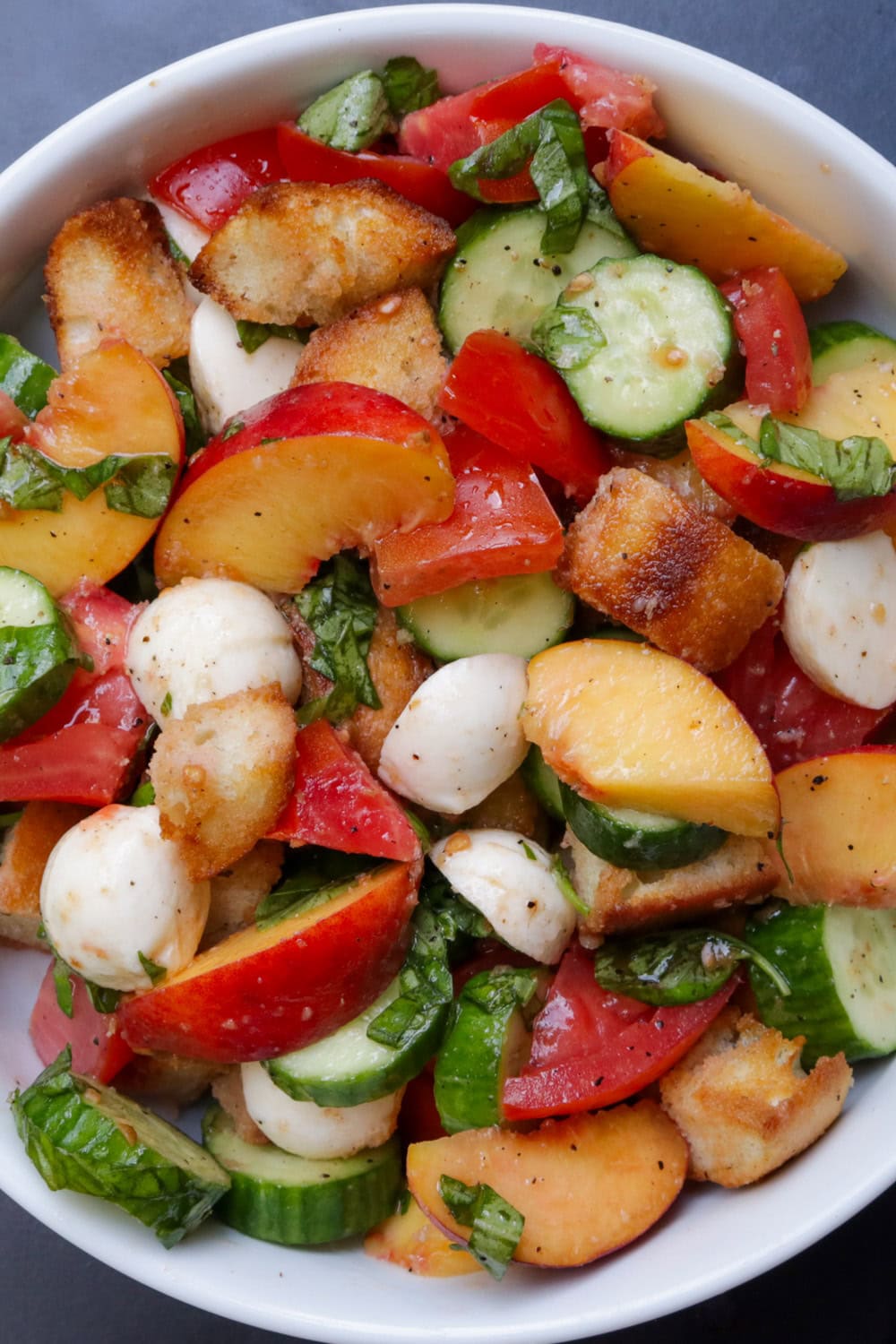 Panzanella bread salad with peaches in white bowl.