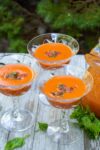 martini glasses with gazpacho on wooden table with pitcher of gazpacho p