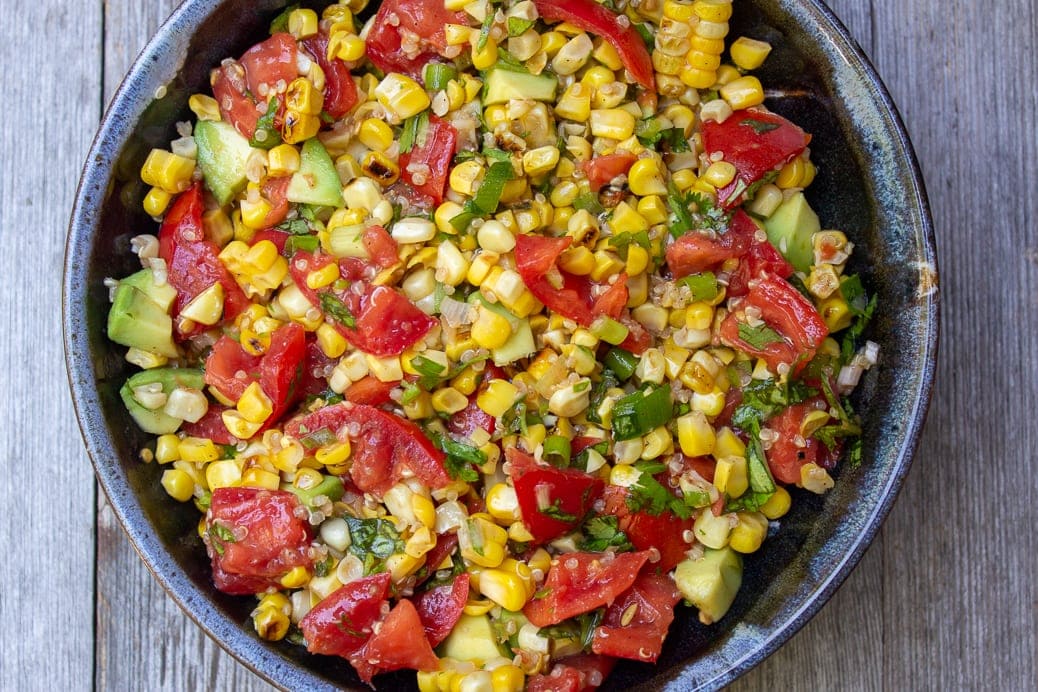 Corn, chopped tomatoes, chopped avocado, chopped herbs and quinoa in bowl mixed together in bowl