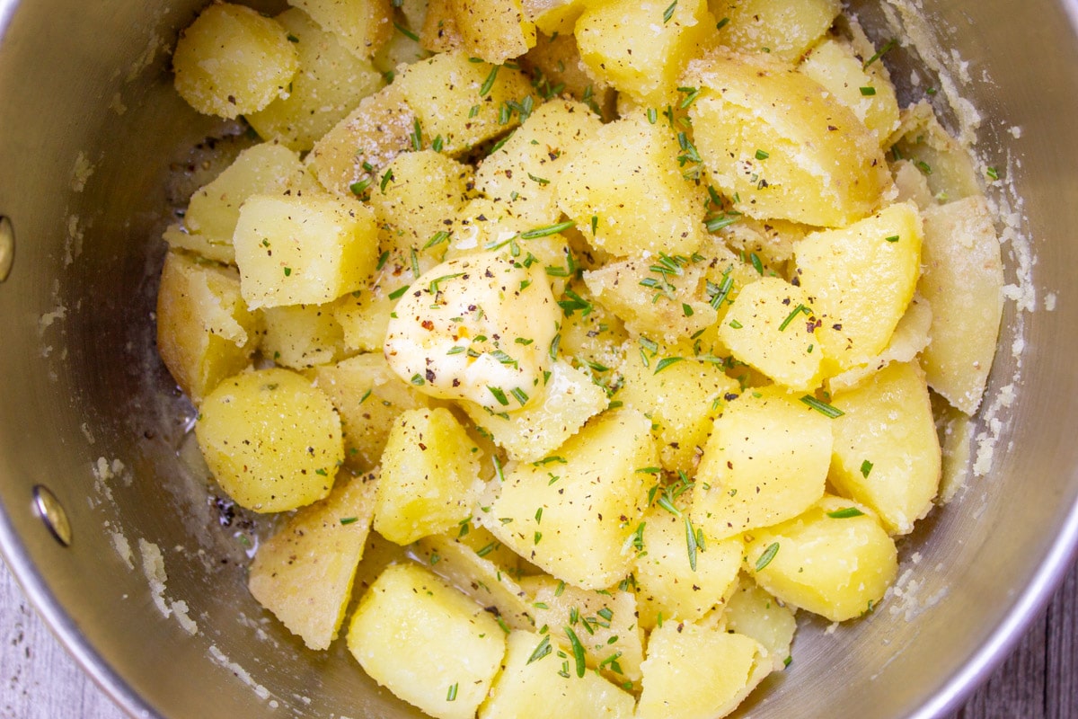 butter and seasonings on boiled potatoes in pot.