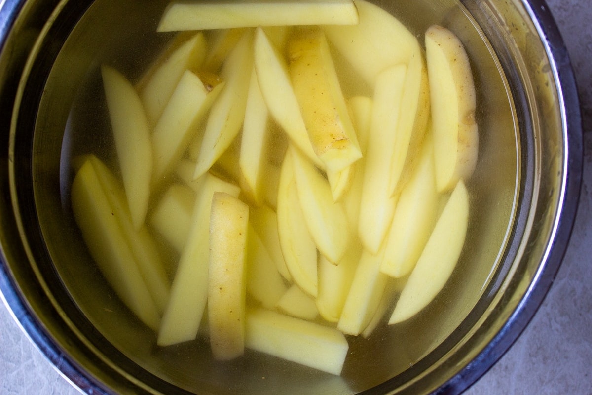 raw cut potatoes soaking in bowl of cold water