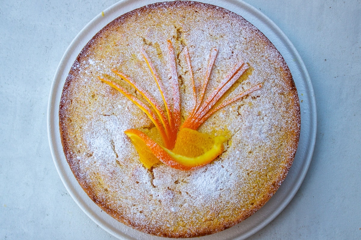 Whole Orange Cake on plate dusted with icing sugar and decorated with orange slice and zest