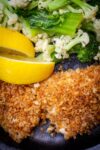 plate of breaded baked fish with vegetables and lemon wedges p