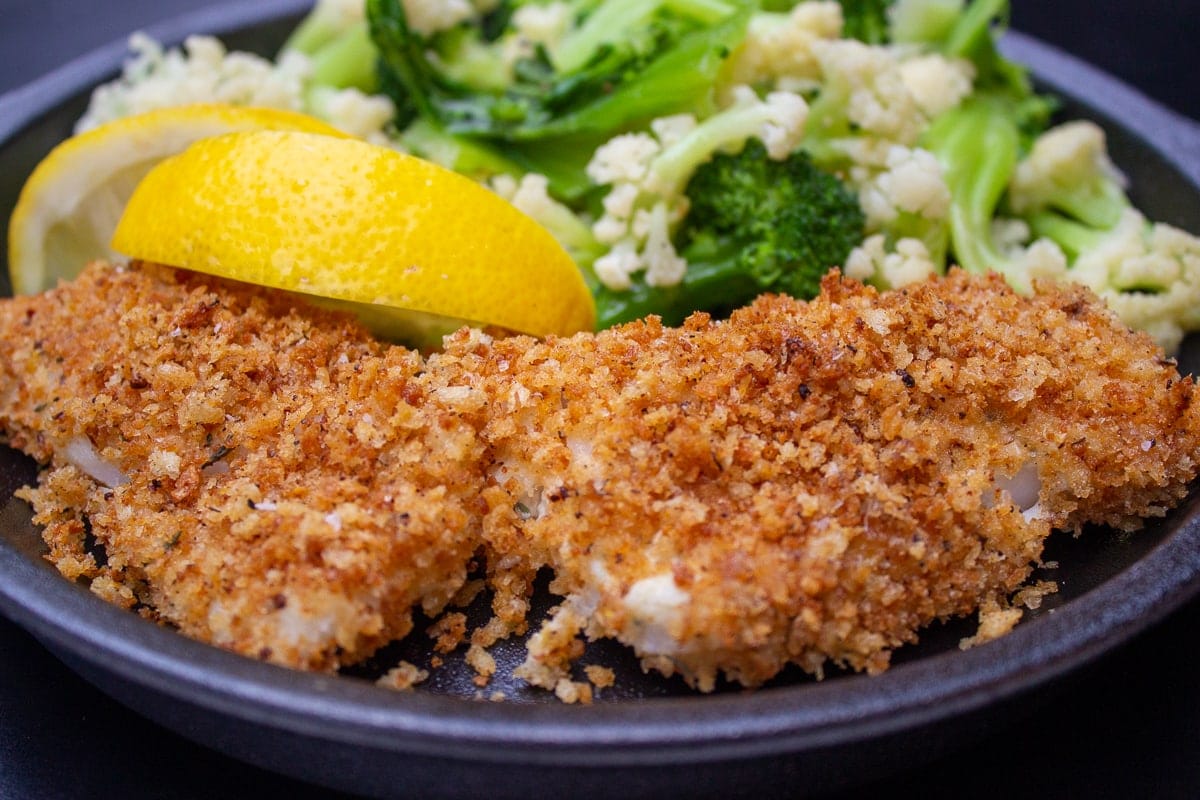 plate of breaded baked fish with vegetables and lemon wedges 1