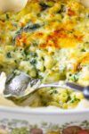 spoon scooping baked spinach mac and cheese from casserole dish.
