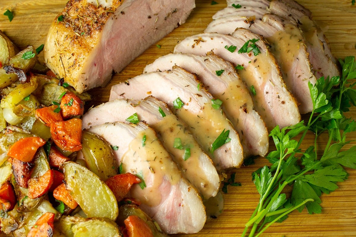 sliced pork roast on cutting board with gravy and potatoes