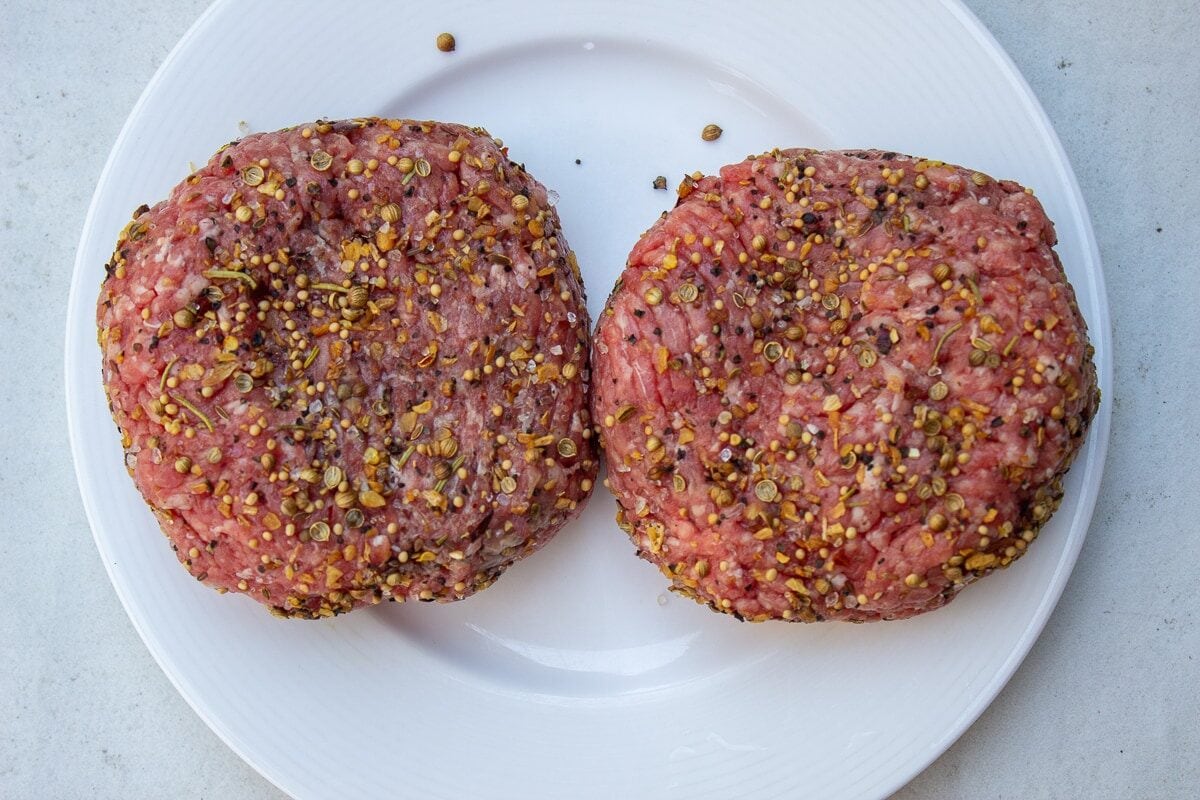 2 raw seasoned burgers on plate.