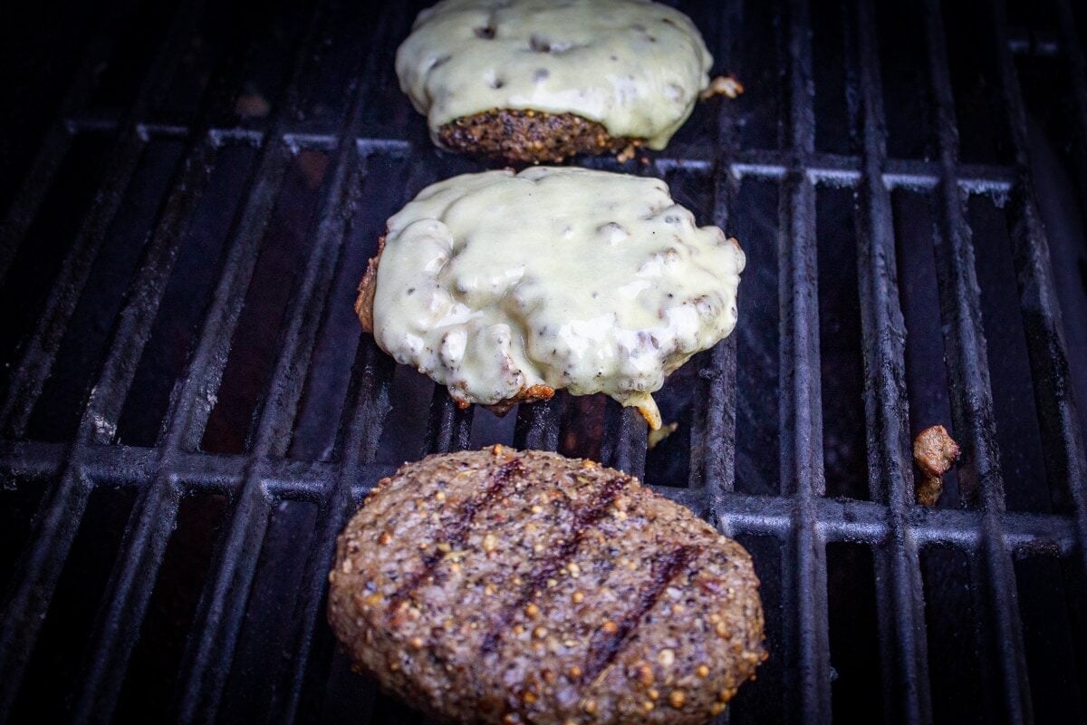 3 sous vide burgers (two with melted cheese) grilling on grill.
