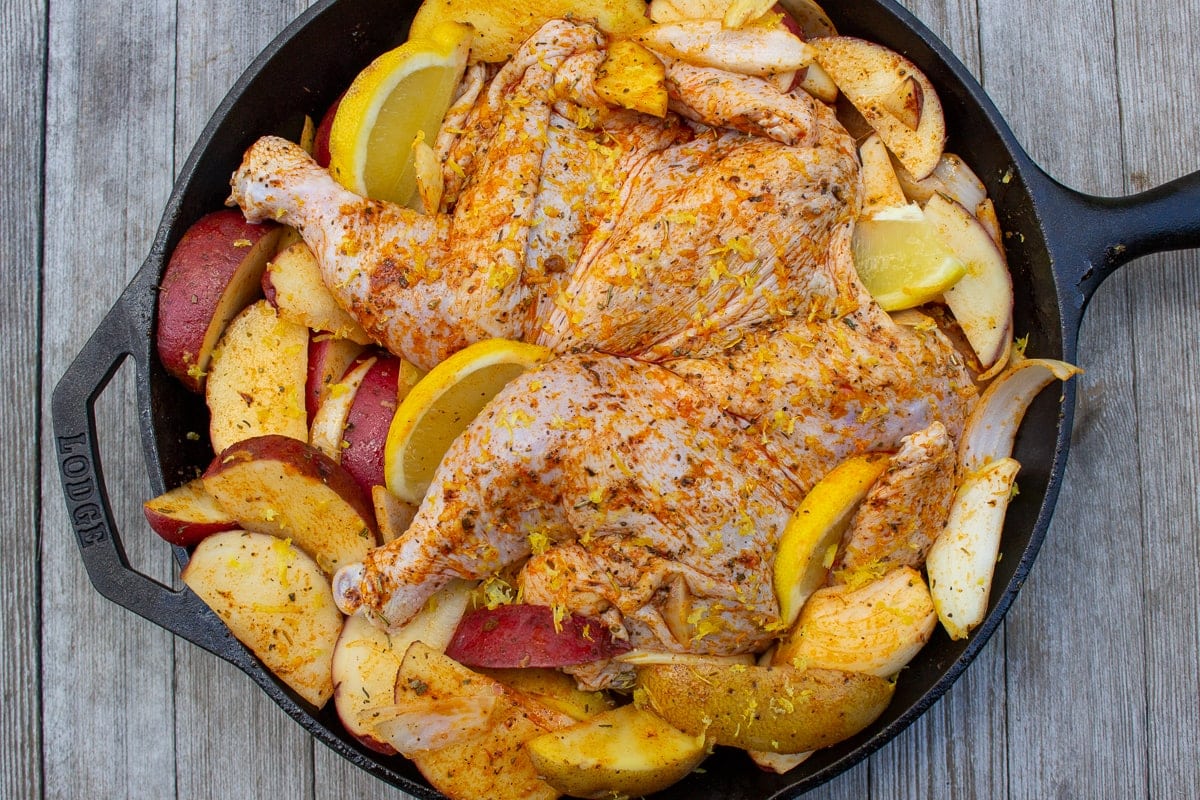 uncooked chicken, potatoes and lemon in skillet