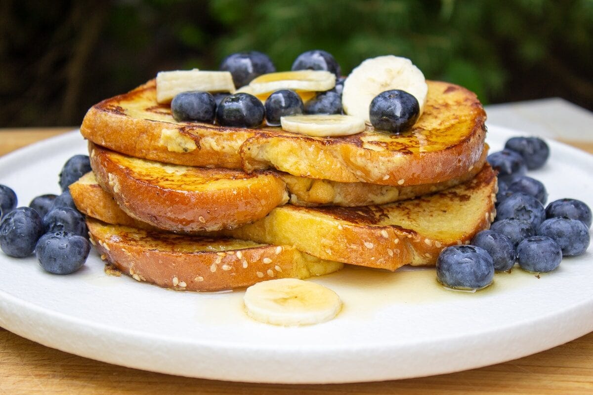 stack of banana French toast on plate with berries and banana slices