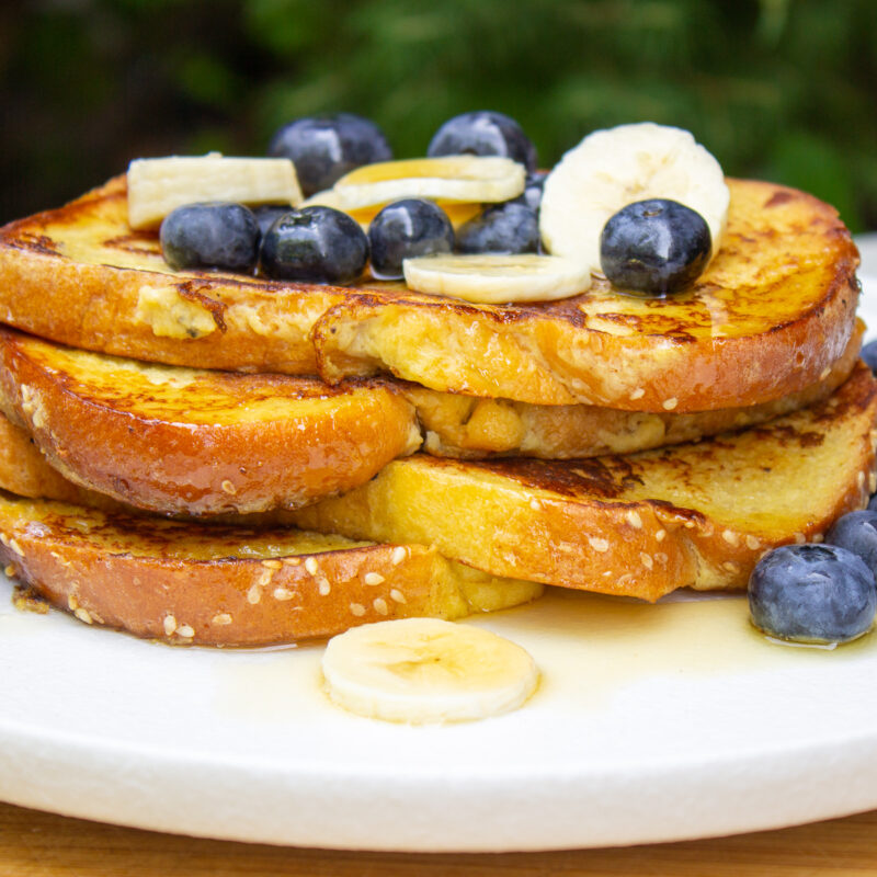 stack of banana french toast on plate with fresh fruit on top