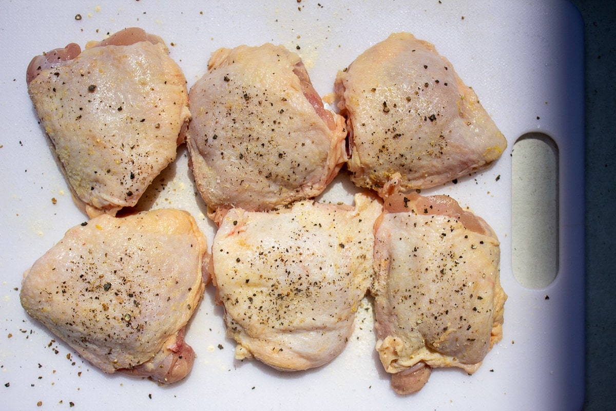 6 raw seasoned chicken thighs on cutting board