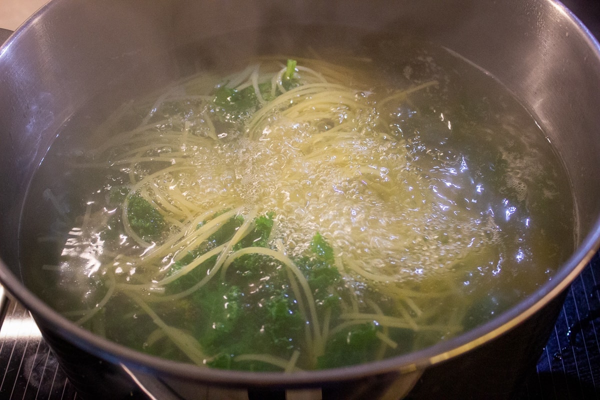 spaghetti and kale in boiling water in pot