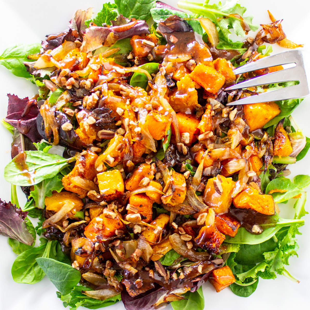 butternut squash salad with caramelized onions over greens on plate.