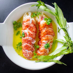 2 lobster tails in butter in dish with tarragon