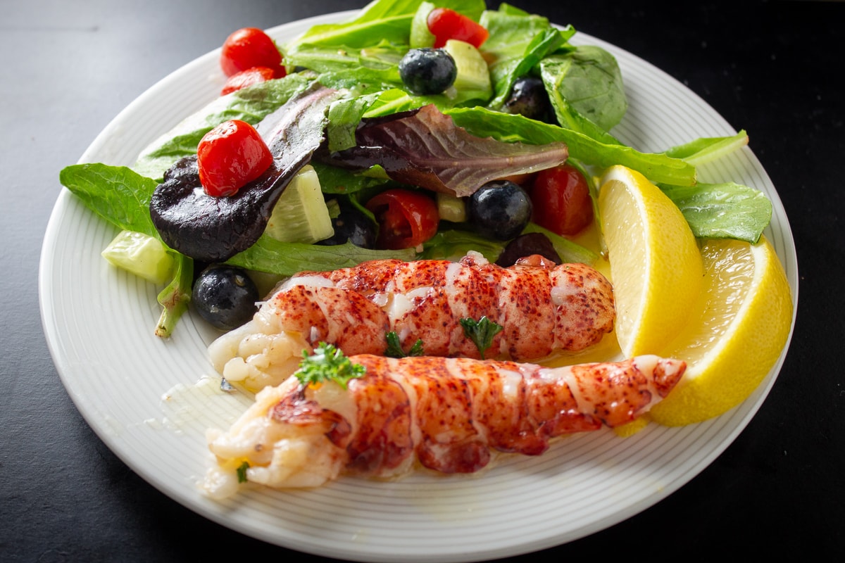 2 lobster tails on plate with salad and lemon