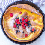 dutch pancake in skillet with dusted sugar and berries on top