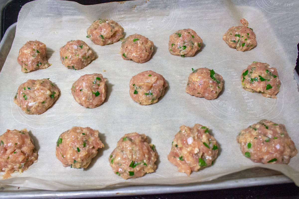 uncooked meatballs on parchment lined sheet pan 