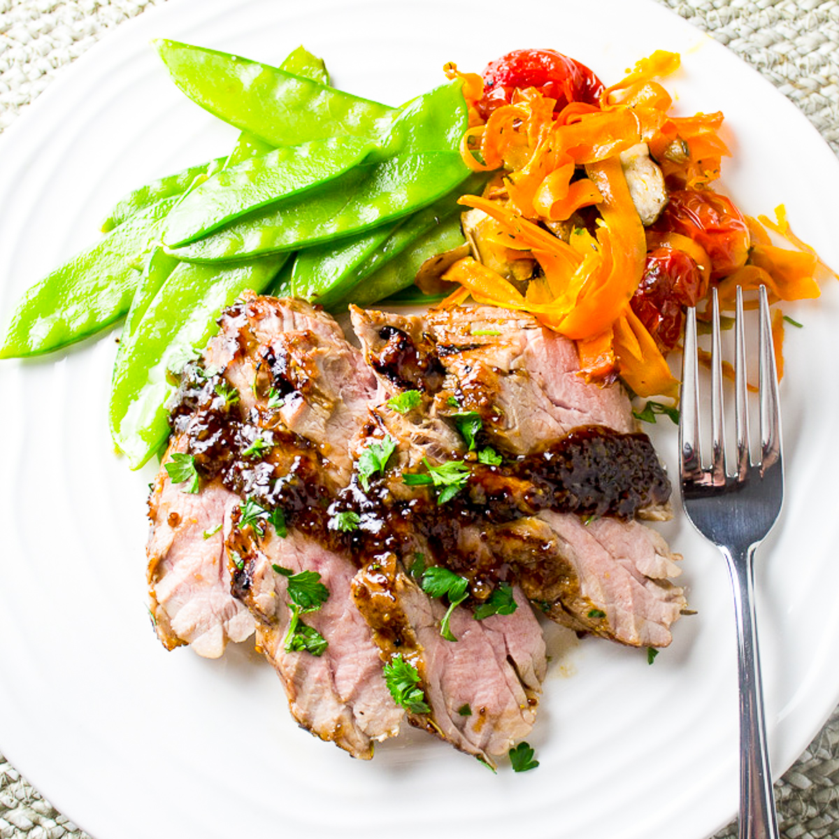 sliced pork tenderloin with snow peas and roasted veggies on plate with sauce