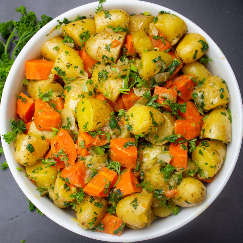 bowl of cooked potatoes and carrots with herbs on black table
