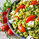 pesto pasta with veggies in bowl with tomatoes beside it