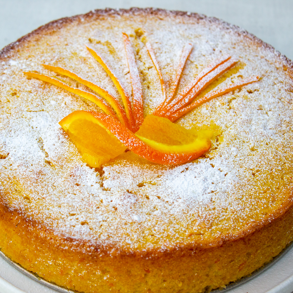 whole orange cake on white plate dusted with icing sugar and orange strips