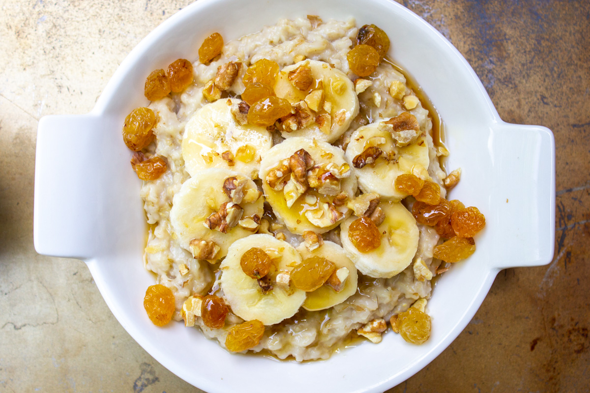 bowl of oatmeal topped with bananas raisins maple syrup nuts