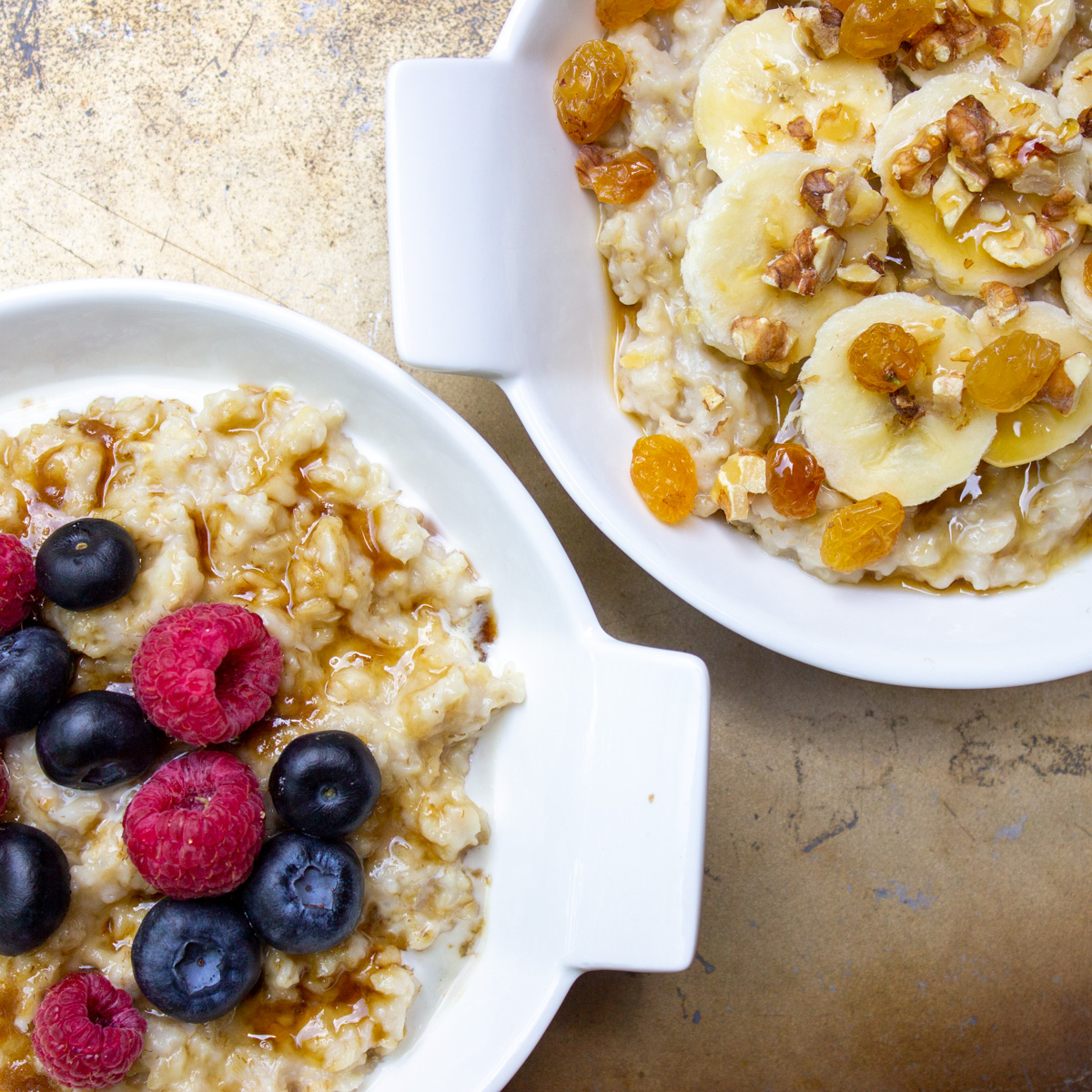 2 bowls of oatmeal, one with berries, one with bananas and raisins and nuts