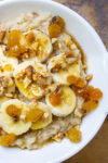 bowl of oatmeal topped with bananas raisins maple syrup nuts p1