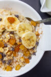 bowl of oatmeal topped with bananas raisins maple syrup chocolate chips nuts p