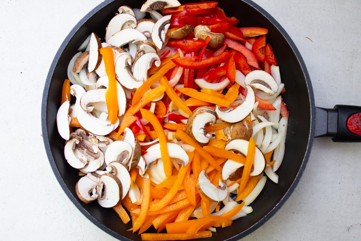 skillet with raw onions mushrooms, peppers