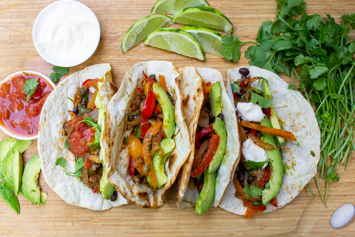 4 filled fajitas on cutting board with condiments