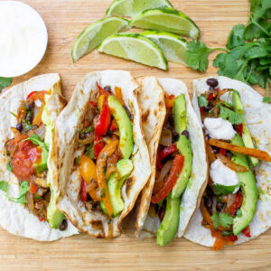 4 filled fajitas on cutting board with condiments f