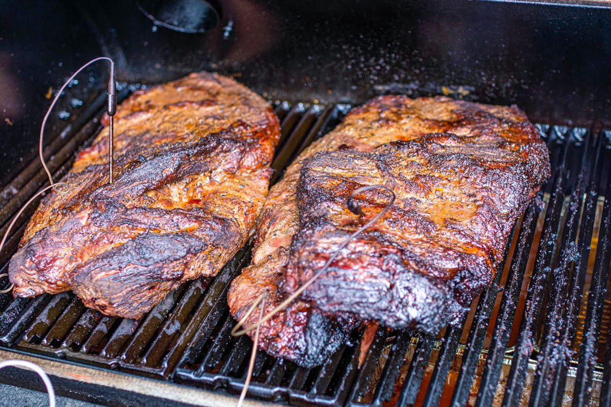two briskets cooking on grill with sensor prods in them