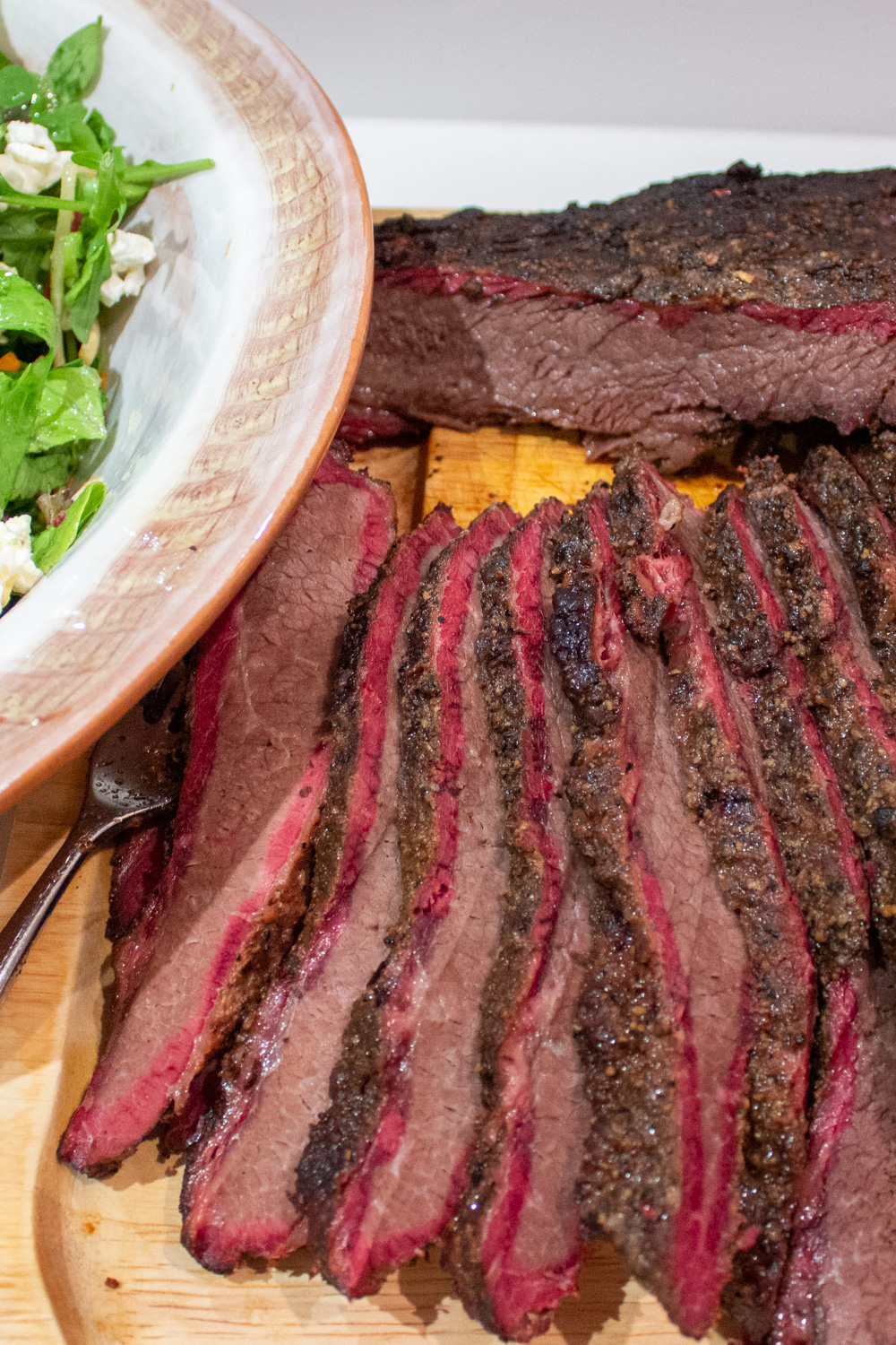 sliced smoked brisket on cutting board beside bowl of salad p