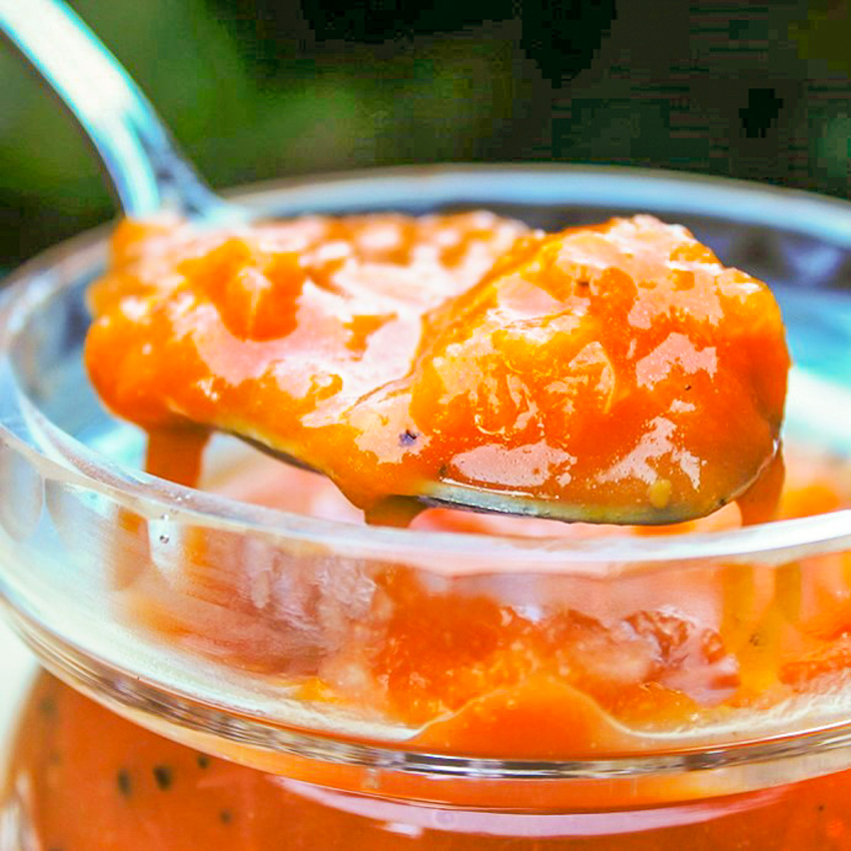 peach sauce on spoon over jar of serving jar of peach sauce