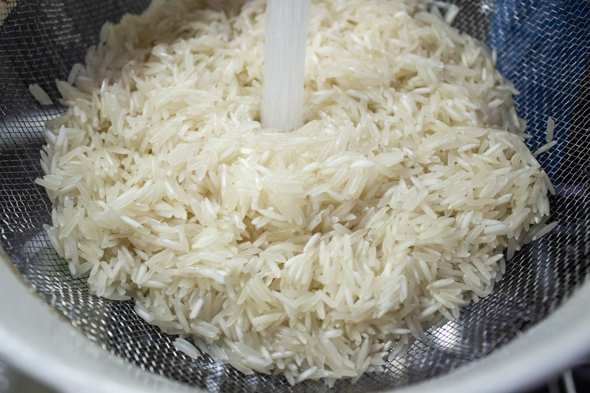 raw rice in sieve under running water
