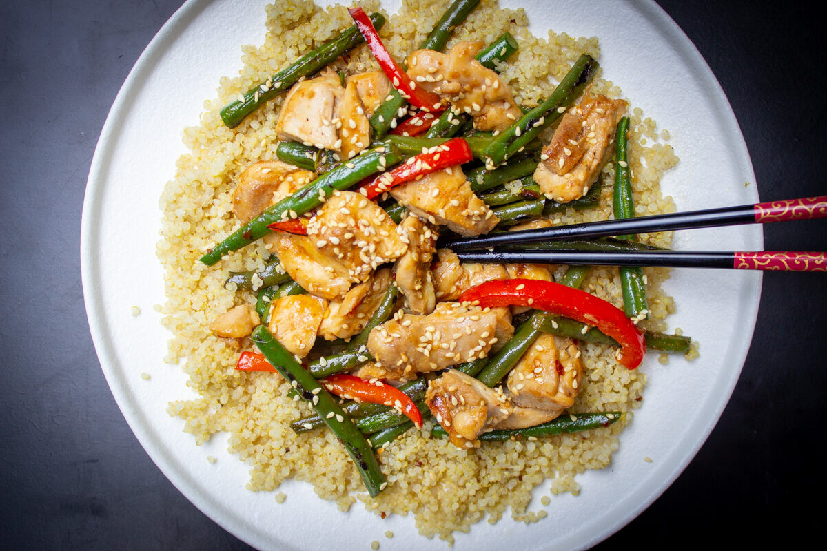 chicken and green bean stir fry on plate over quinoa with sesame seeds