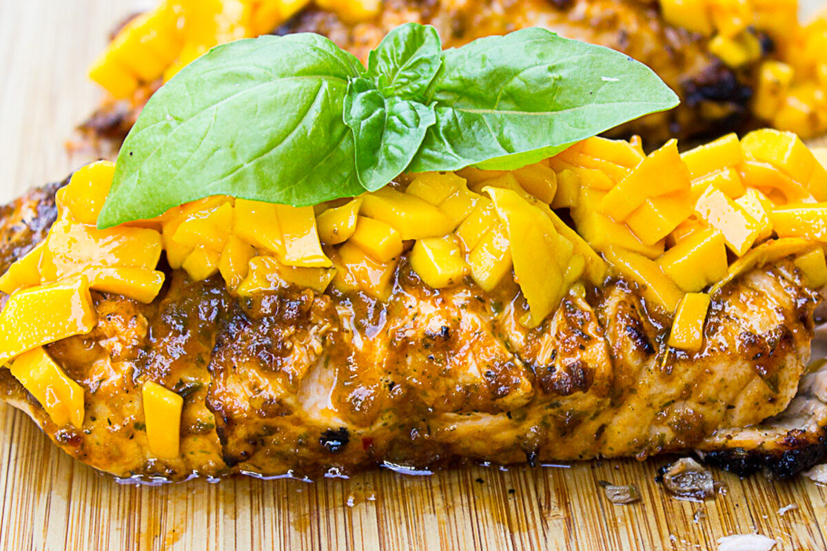 two salmon fillets with basil topped with mango on cutting board with leaf on top