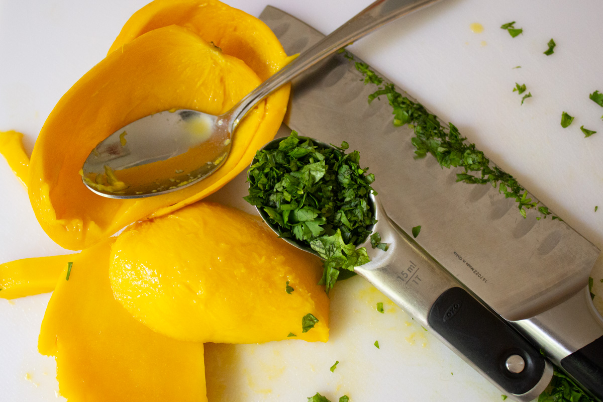 mango flesh out of skin and chopped cilantro in a spoon