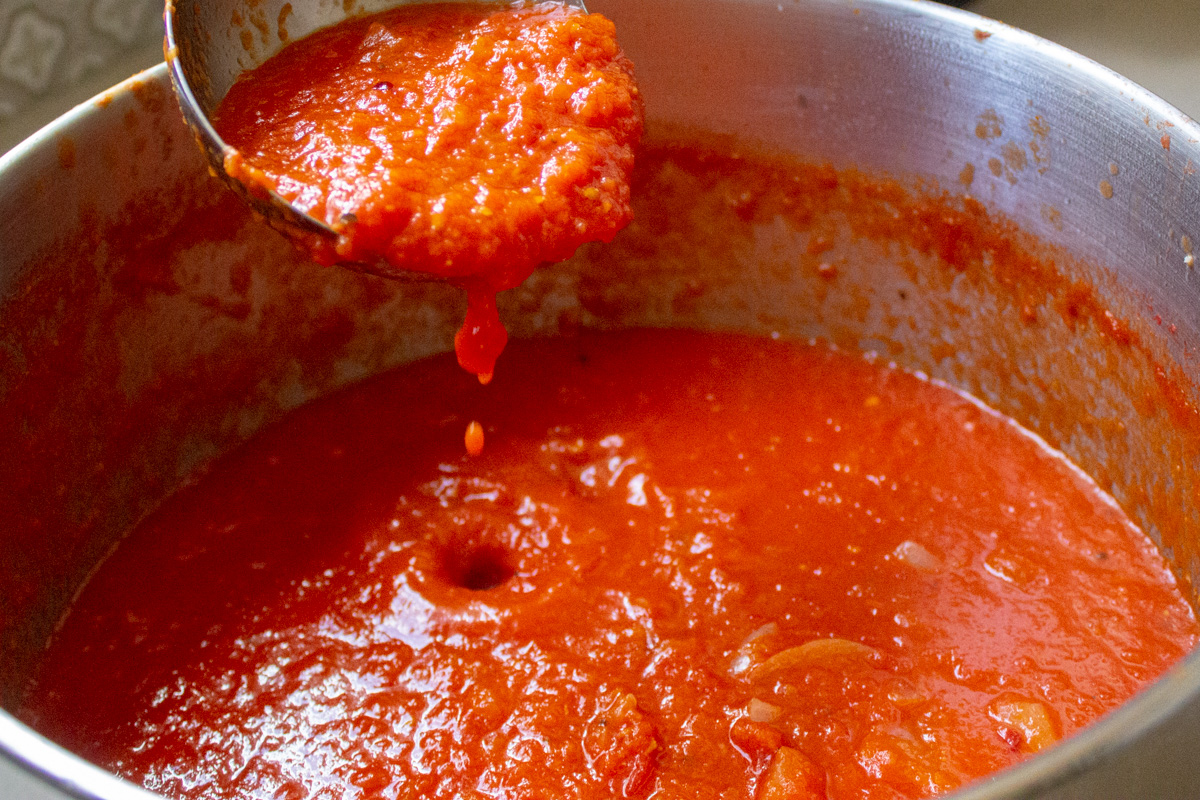 ladle of san marzano tomato sauce over pot 