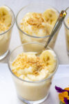 4 glass cups with pudding topped with graham crumbs and a banana slice