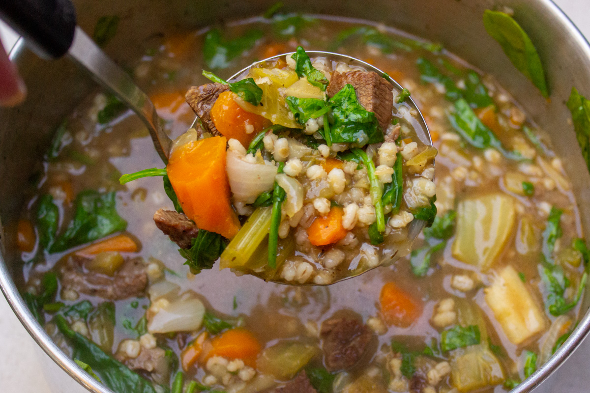 finished beef barley vegetable soup in pot with ladle holding up a scoop