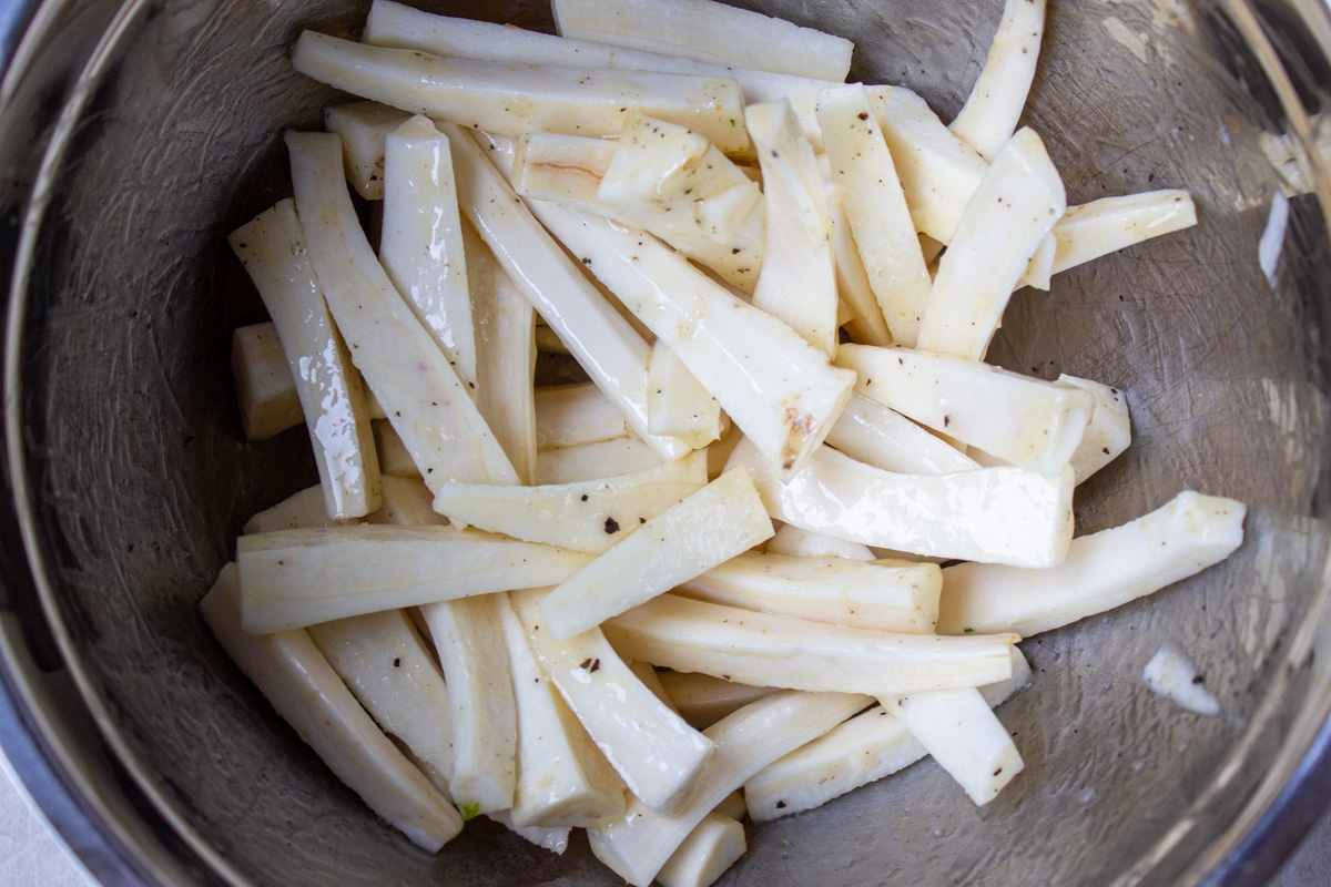 parsnips cut in sticks in bowl with oil and honey