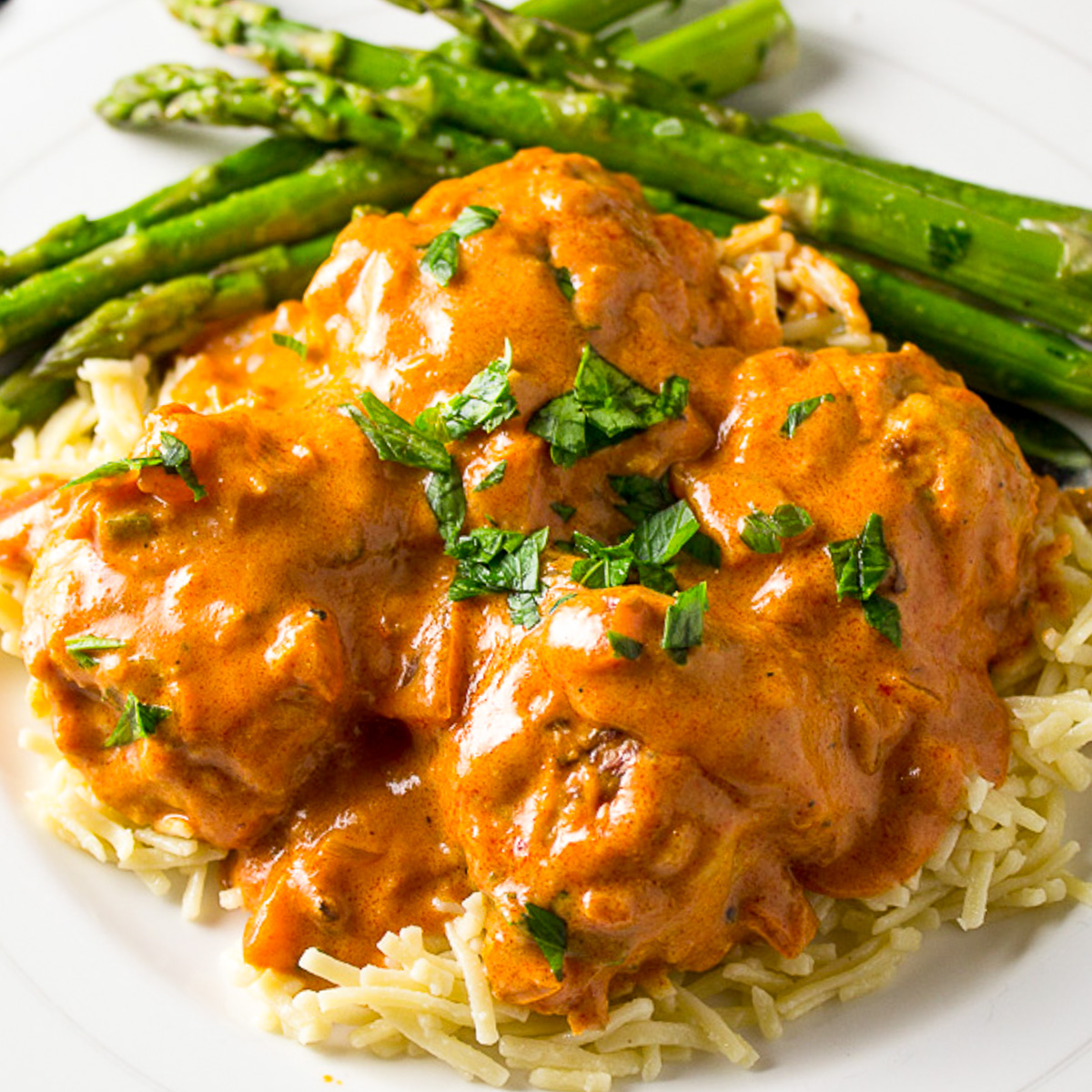 chicken meatball paprikash over egg noodles on plate with asparagus