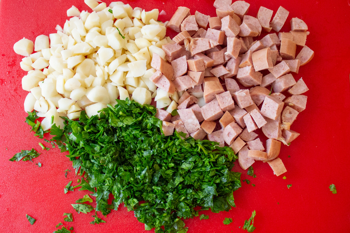 chopped hot dogs, water chestnuts and parsley on red cutting board.